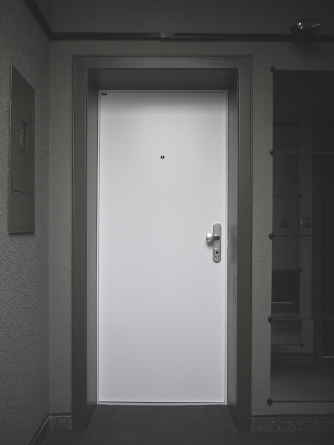 Weiße, flächenbündige Wohnungstür in einer erhaltenen dunkelgrauen Zarge